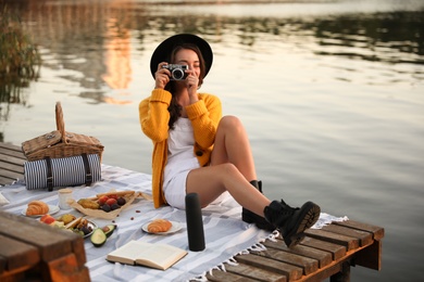 Photo of Young woman taking picture with camera on pier at picnic