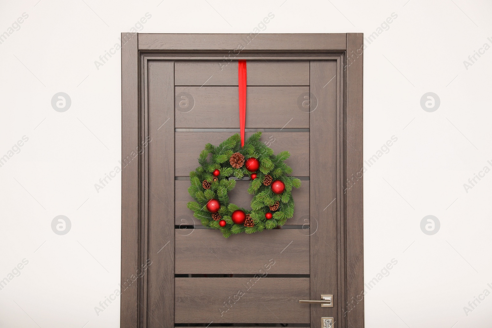 Photo of Christmas wreath with red baubles and cones hanging on wooden door indoors
