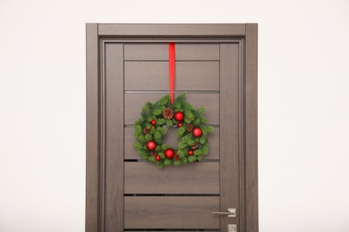 Christmas wreath with red baubles and cones hanging on wooden door indoors
