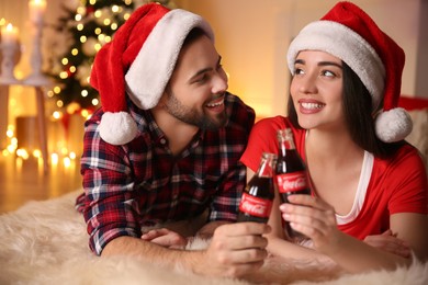 Photo of MYKOLAIV, UKRAINE - JANUARY 27, 2021: Young couple holding bottles of Coca-Cola at home. Christmas atmosphere