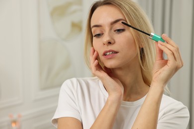 Beautiful woman applying mascara indoors, space for text
