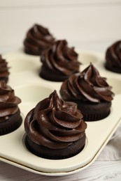 Delicious chocolate cupcakes with cream in baking tray on white wooden table, closeup