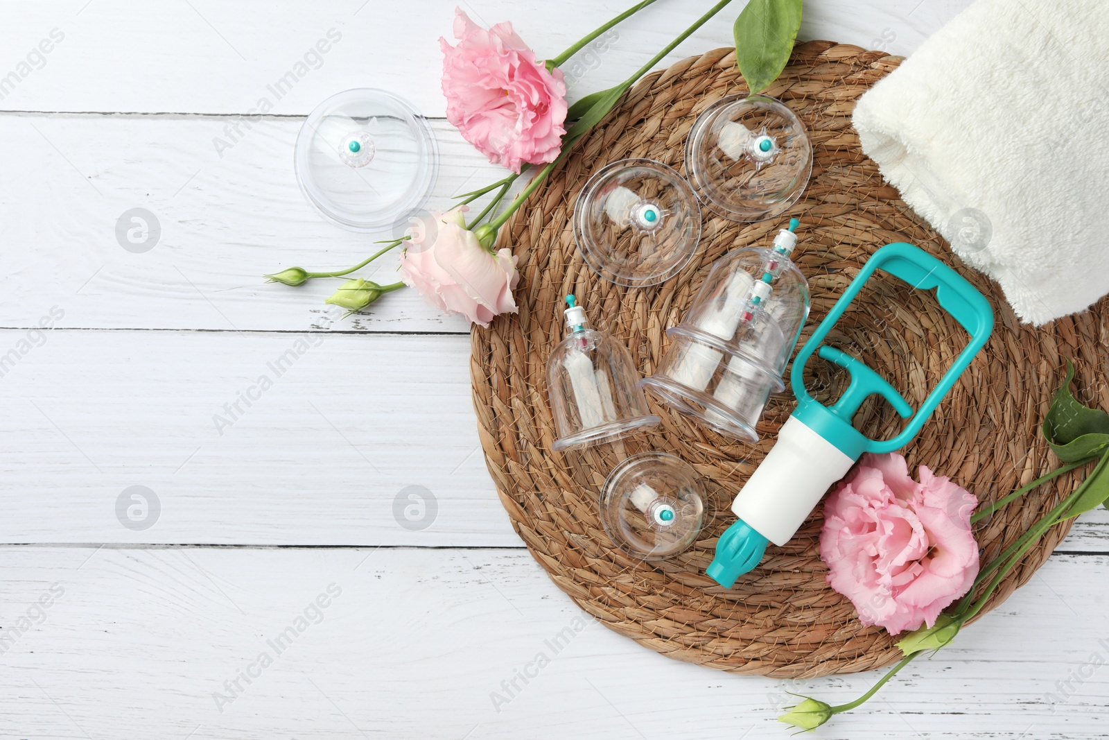 Photo of Plastic cups, hand pump, towel and flowers on white wooden table, flat lay with space for text. Cupping therapy