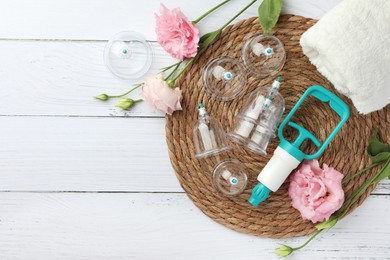 Photo of Plastic cups, hand pump, towel and flowers on white wooden table, flat lay with space for text. Cupping therapy