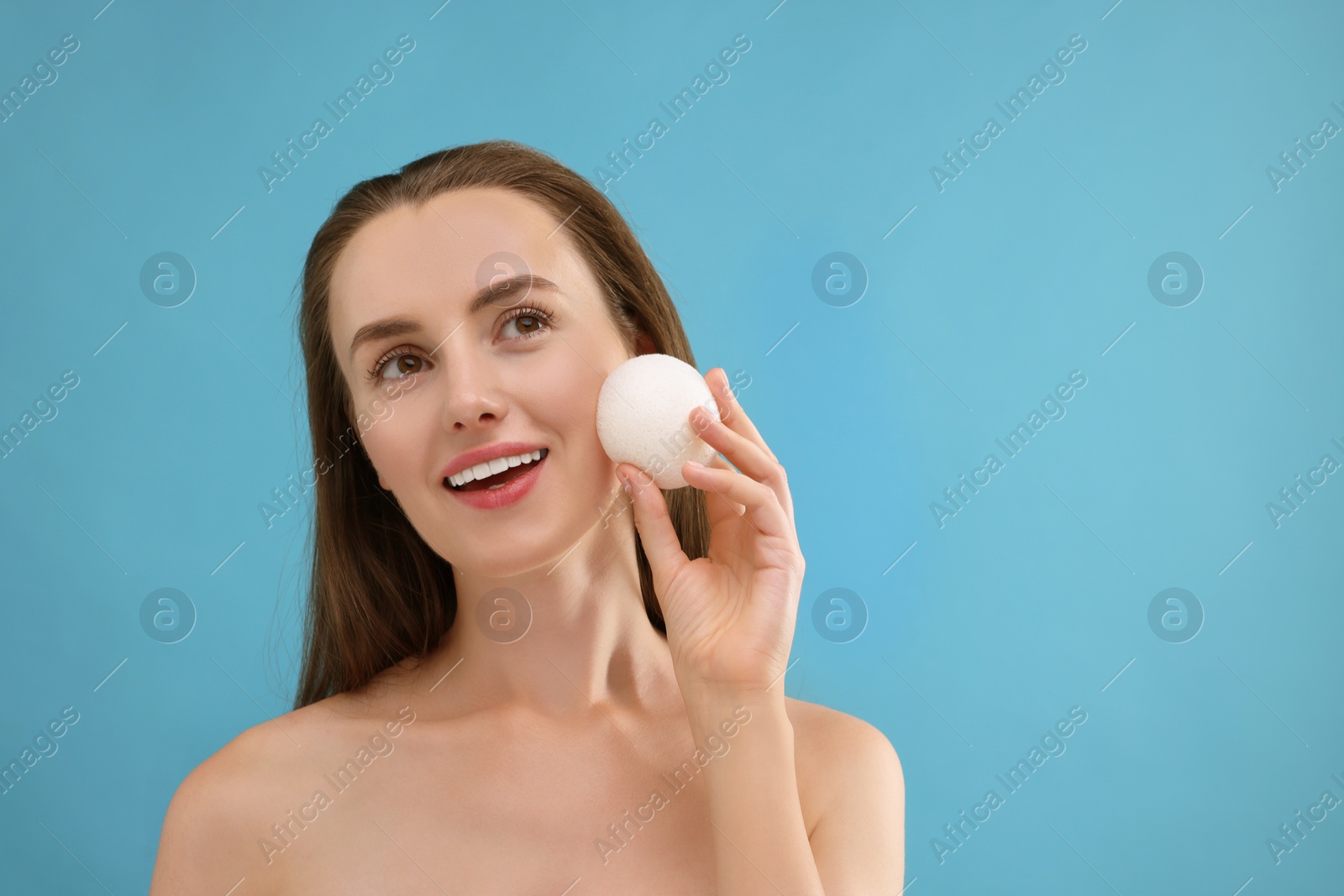 Photo of Happy young woman holding face sponge on light blue background. Space for text