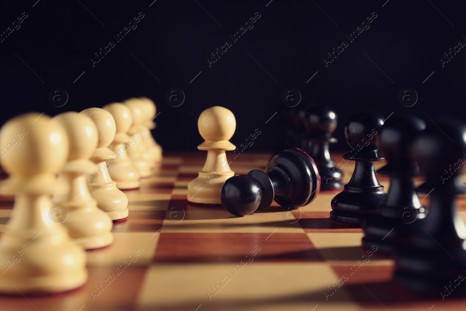 Photo of Black and white pawns on chessboard against dark background, closeup. Competition concept
