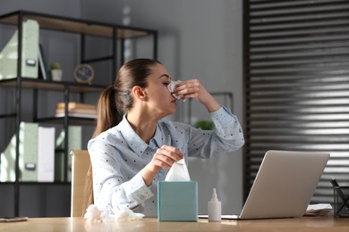 Photo of Ill businesswoman at table with nasal spray and box of paper tissues in office