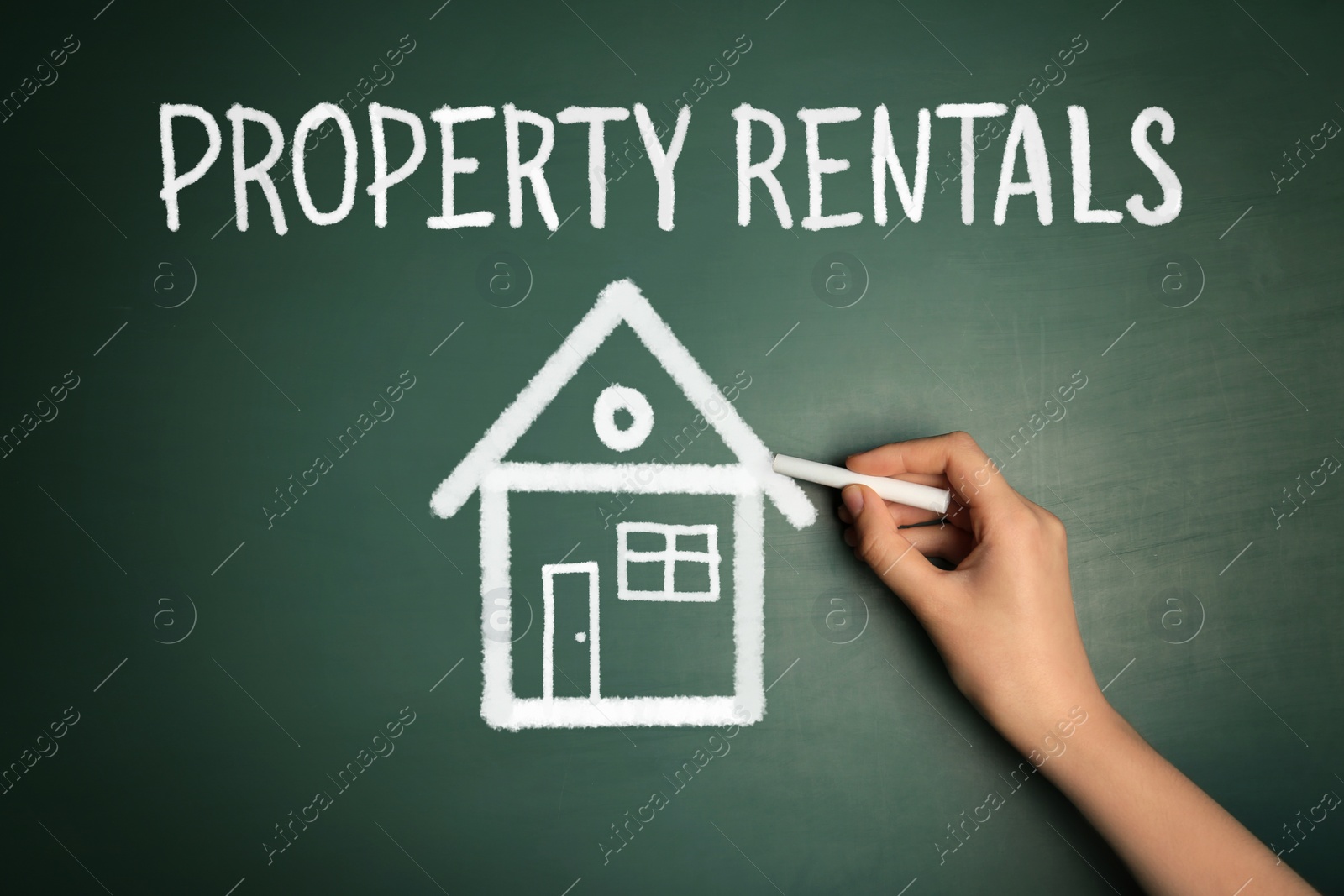 Image of Woman drawing house near text Property Rentals on green chalkboard, closeup