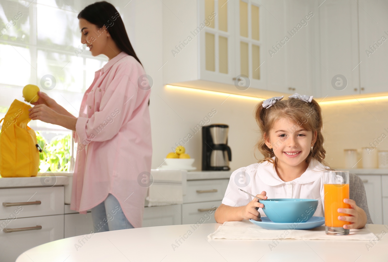 Photo of Little girl having breakfast while mother helping her get ready for school in kitchen