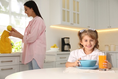 Photo of Little girl having breakfast while mother helping her get ready for school in kitchen