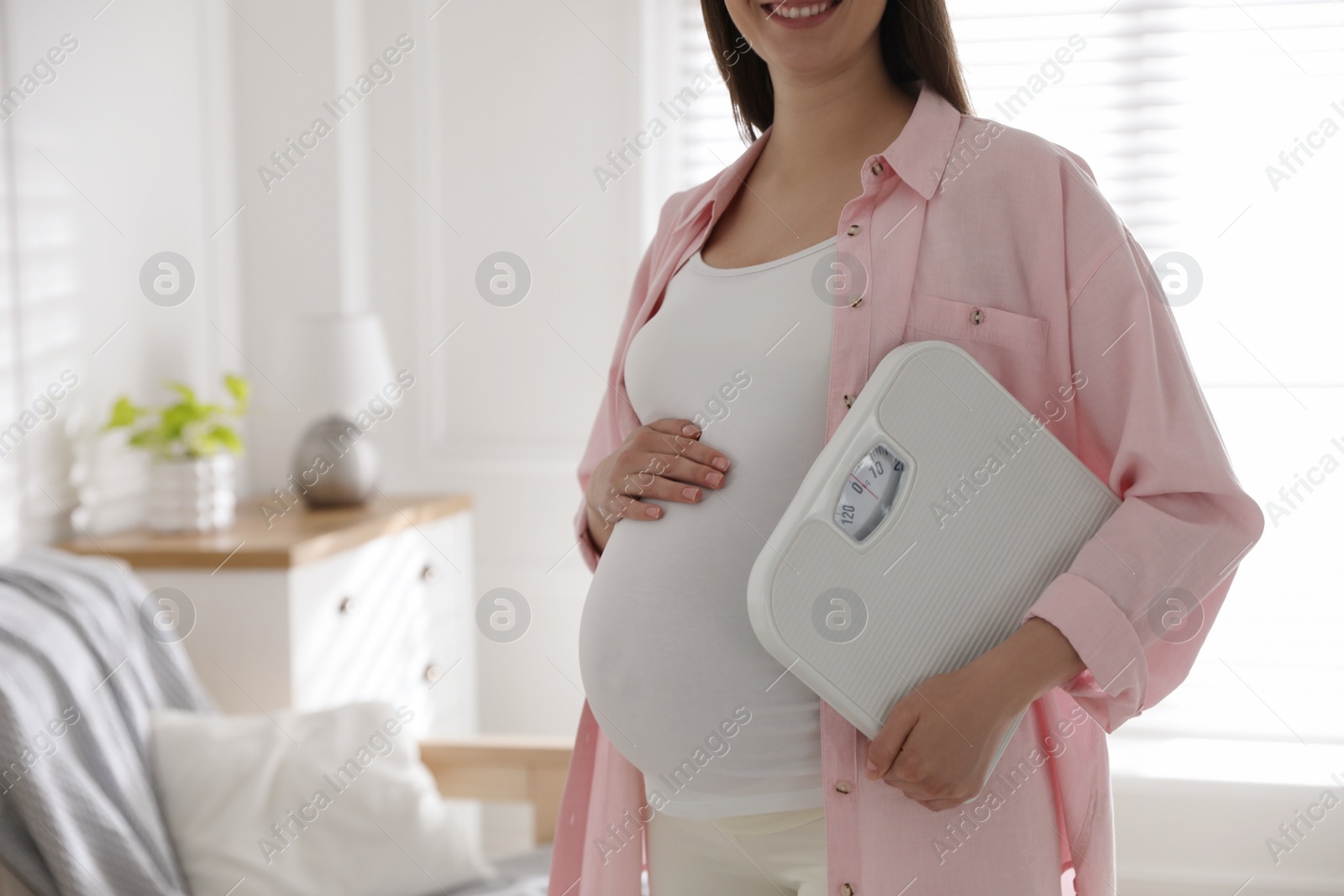 Photo of Young pregnant woman with scales at home, closeup