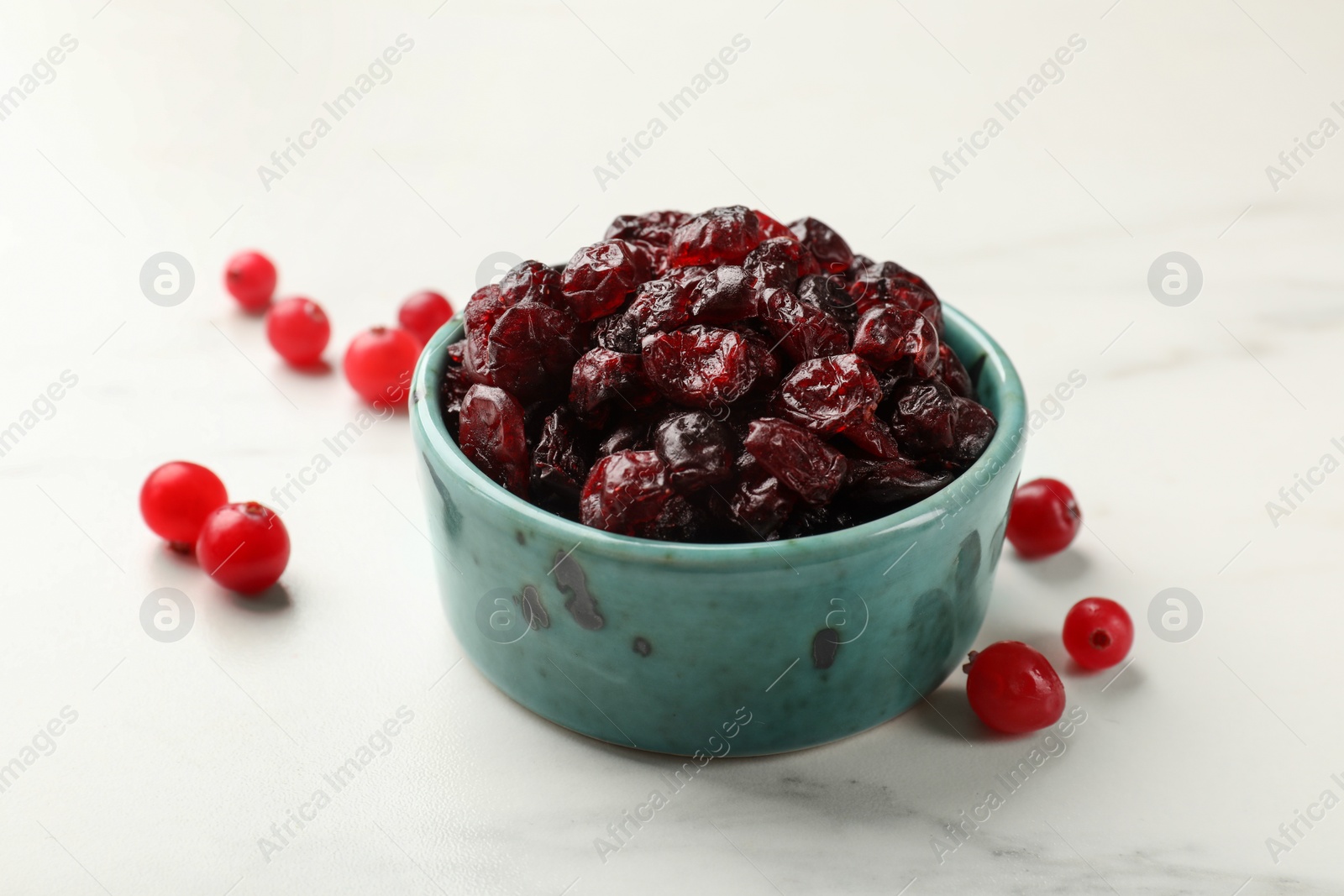 Photo of Tasty dried cranberries in bowl and fresh ones on white marble table, closeup