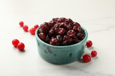 Tasty dried cranberries in bowl and fresh ones on white marble table, closeup