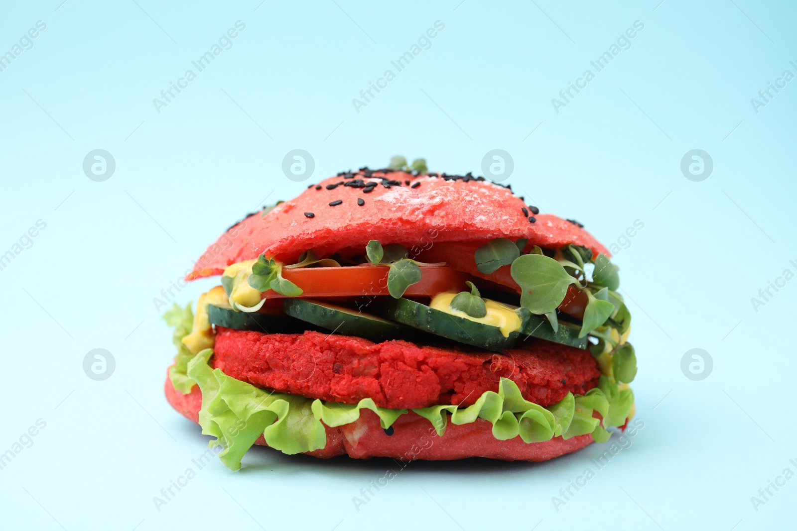 Photo of Tasty pink vegan burger with vegetables, patty and microgreens on light blue background, closeup