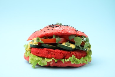 Photo of Tasty pink vegan burger with vegetables, patty and microgreens on light blue background, closeup