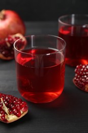 Photo of Tasty pomegranate juice in glasses and fresh fruits on black wooden table, closeup