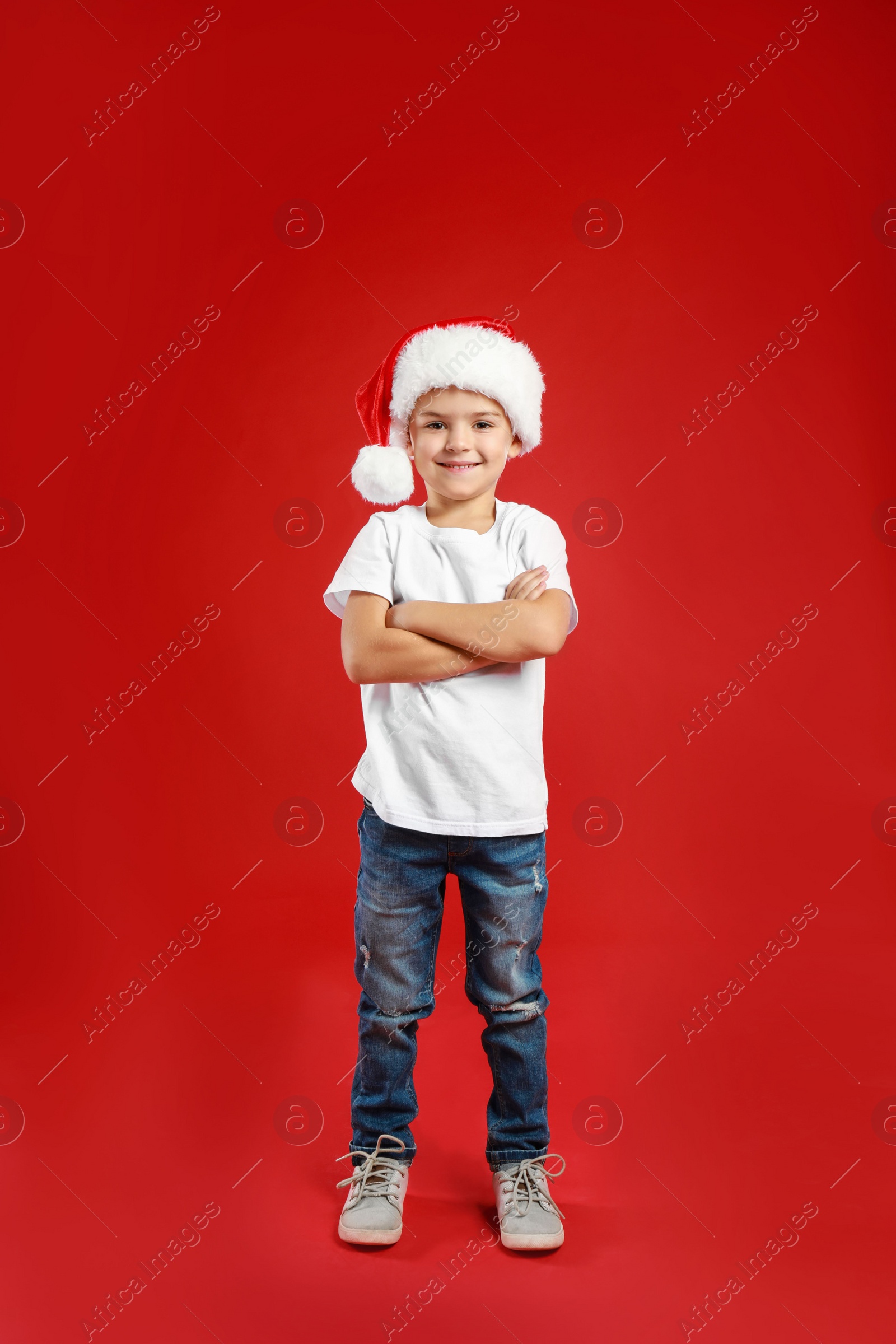 Photo of Cute little child wearing Santa hat on red background. Christmas holiday