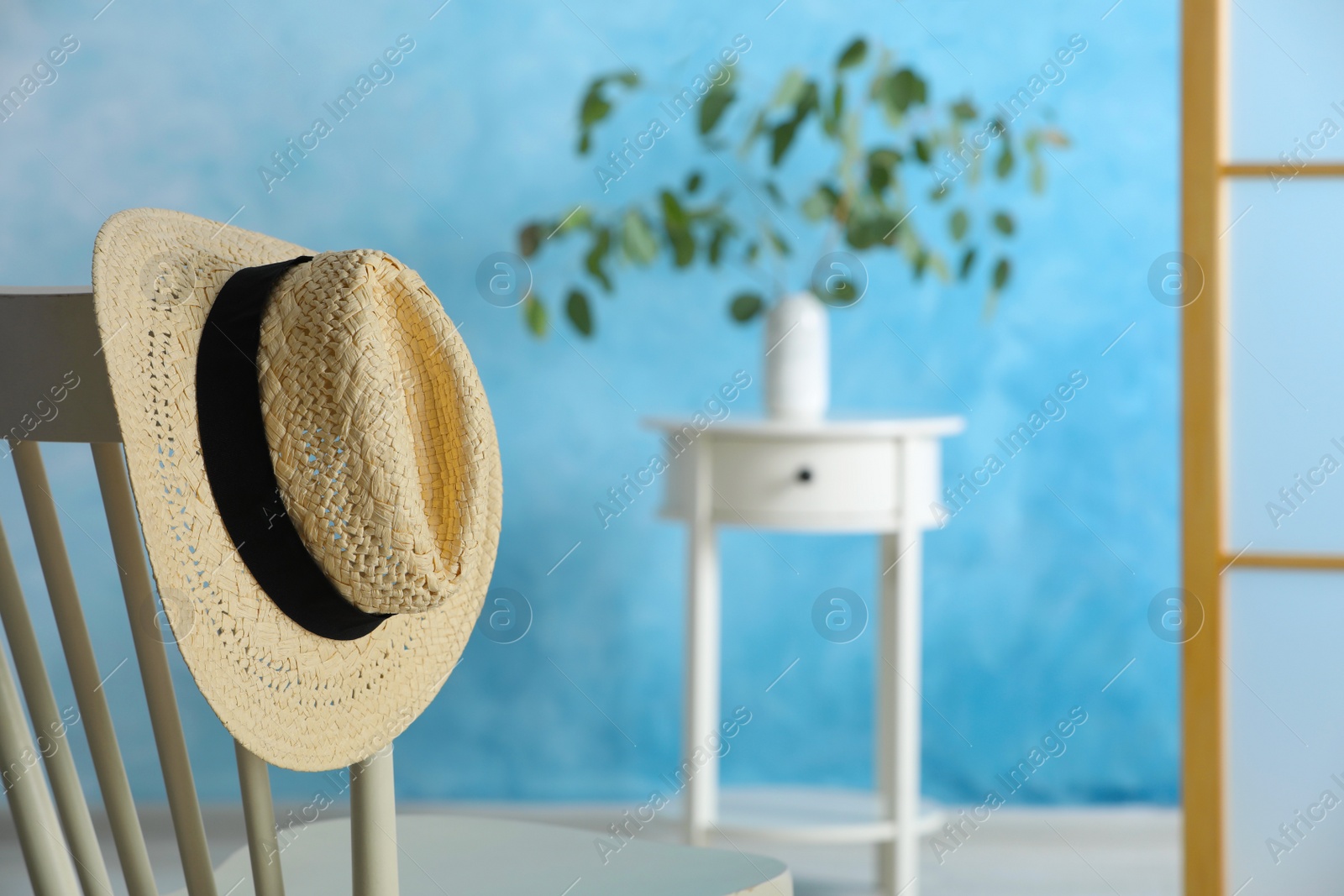 Photo of Stylish straw hat hanging on chair in room, space for text