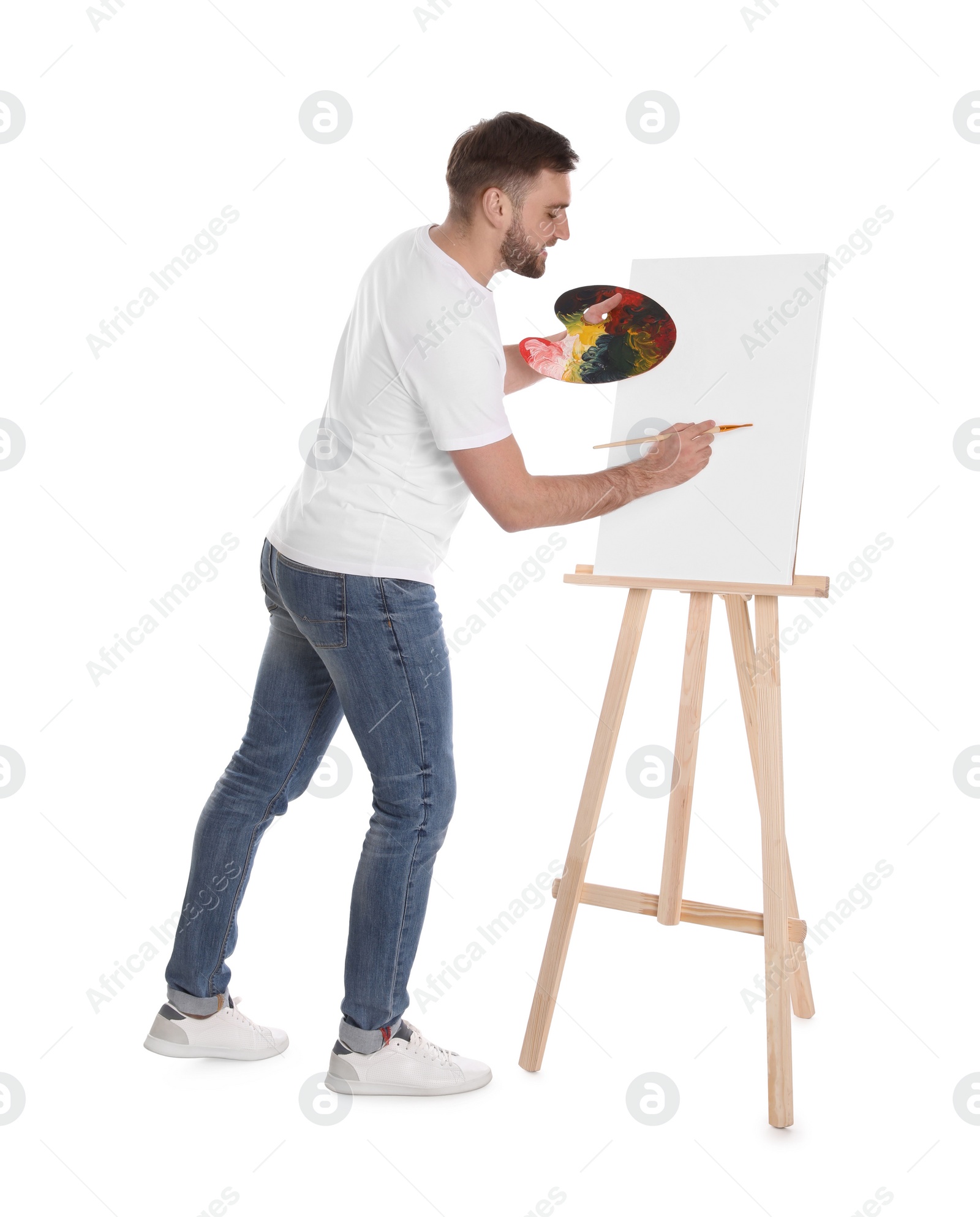 Photo of Man painting with brush on easel against white background. Young artist