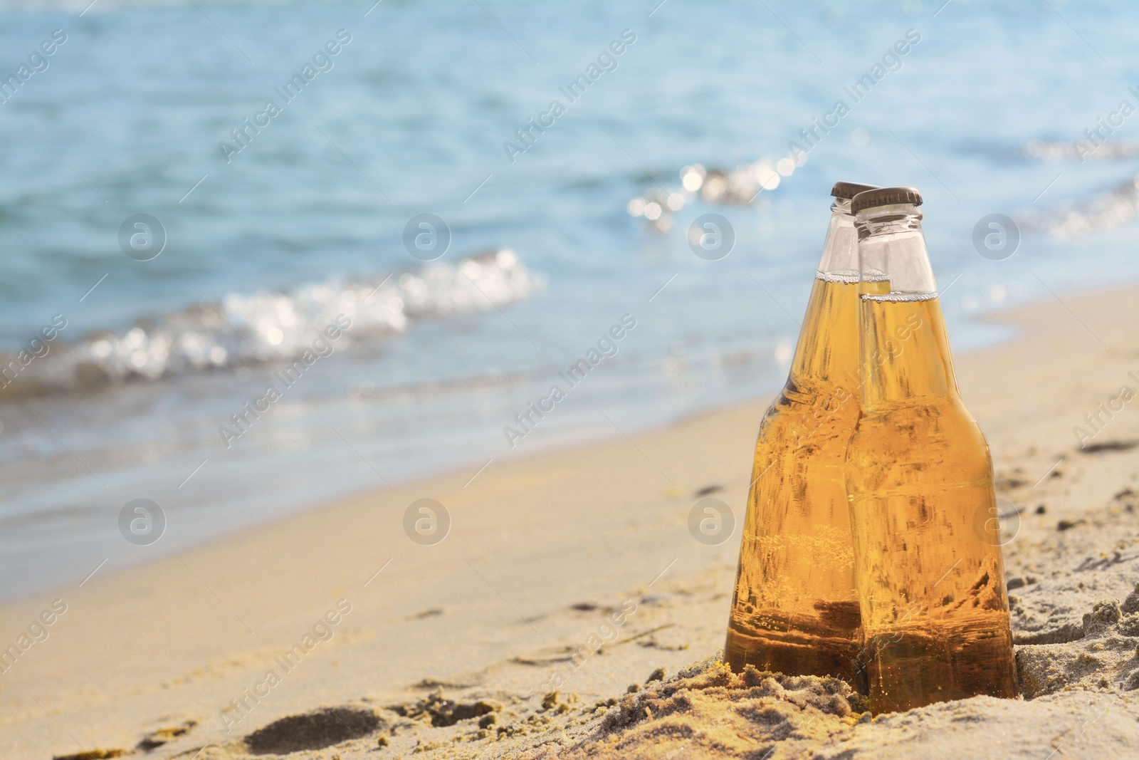 Photo of Bottles of cold beer on sandy beach near sea, space for text