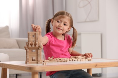 Photo of Cute little girl playing with wooden tower at table indoors. Child's toy