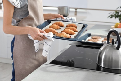 Photo of Young woman holding oven sheet with homemade croissants in kitchen, closeup