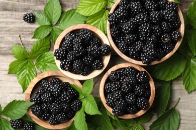 Photo of Ripe blackberries and green leaves on wooden table, flat lay