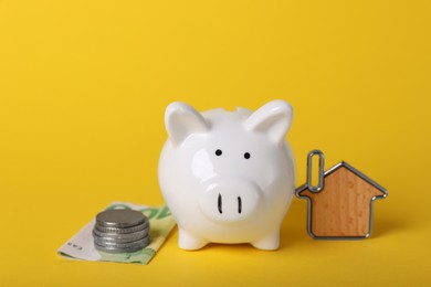 Photo of Ceramic piggy bank, money and key trinket on yellow background. Financial savings