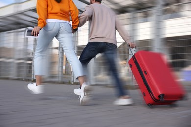 Image of Being late. Couple with suitcase running on station, closeup. Motion blur effect