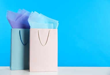 Photo of Gift bags with paper on white table against light blue background, space for text