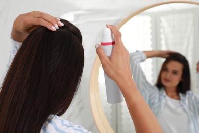 Photo of Woman applying dry shampoo onto her hair near mirror indoors, closeup