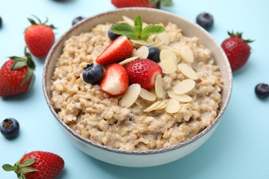 Photo of Tasty oatmeal with strawberries, blueberries and almond flakes in bowl on light blue background, closeup