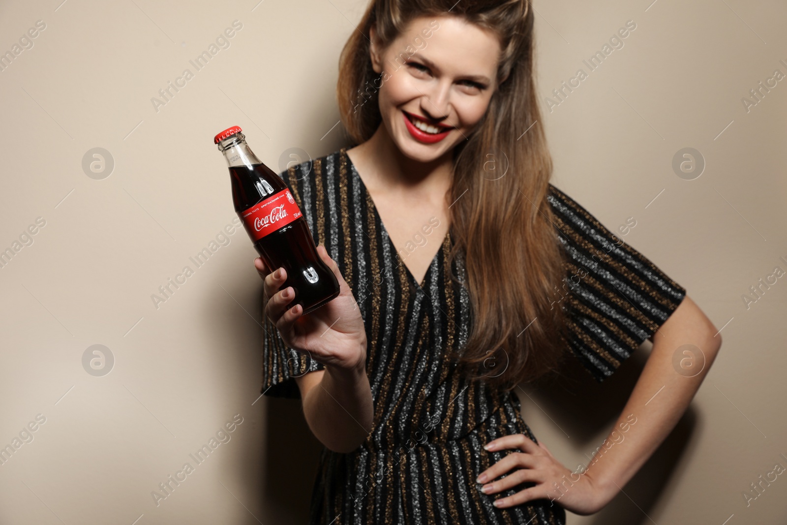 Photo of MYKOLAIV, UKRAINE - NOVEMBER 28, 2018: Young woman with bottle of Coca-Cola on color background