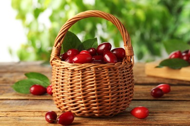 Photo of Fresh ripe dogwood berries with green leaves in wicker basket on wooden table