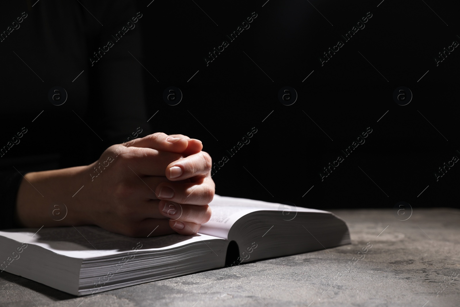 Photo of Religion. Christian woman praying over Bible at table against black background, closeup. Space for text