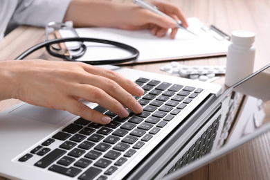 Photo of Doctor working with laptop at desk in office, closeup. Medical service