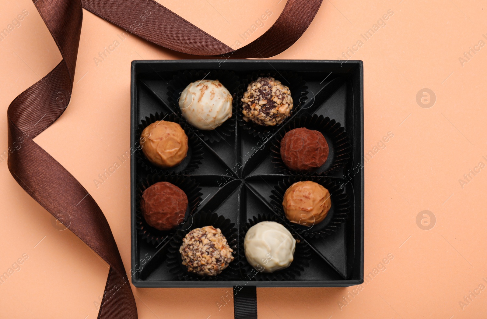 Photo of Box of tasty chocolate candies and ribbon on beige background, flat lay