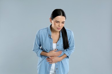 Woman suffering from stomach ache on grey background. Food poisoning