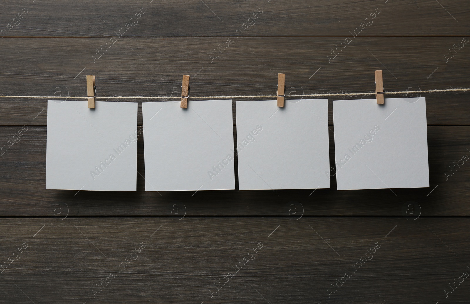 Photo of Clothespins with blank notepapers on twine against wooden background. Space for text