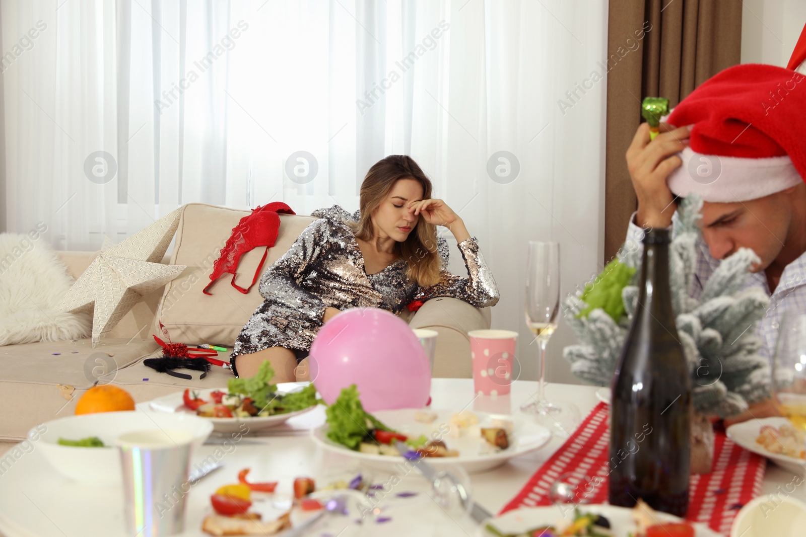 Photo of Woman suffering from hangover in messy room after New Year party