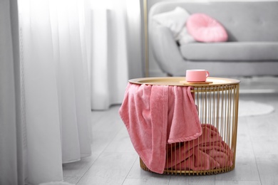 Photo of Side basket table with cup of coffee and blanket in modern room interior