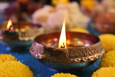 Photo of Diwali celebration. Diya lamp and chrysanthemum flowers on shiny light blue table, closeup