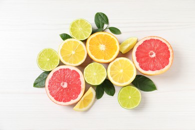 Photo of Different cut citrus fruits and leaves on white wooden table, flat lay