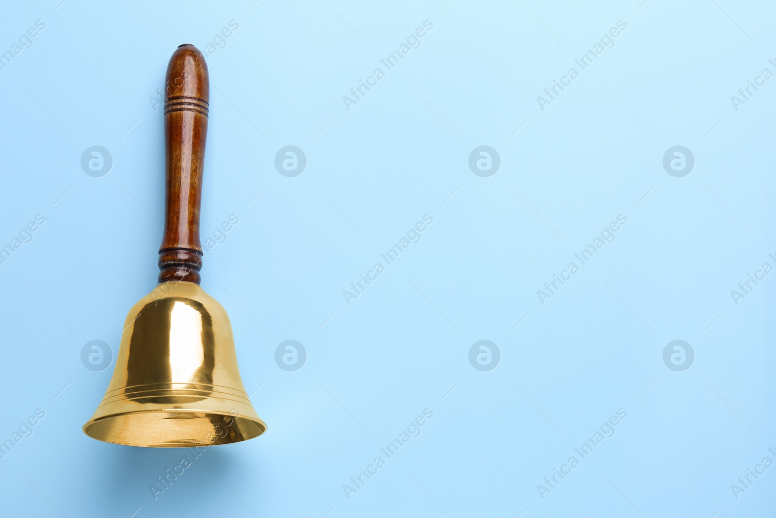 Photo of Golden school bell with wooden handle on light blue background, top view. Space for text