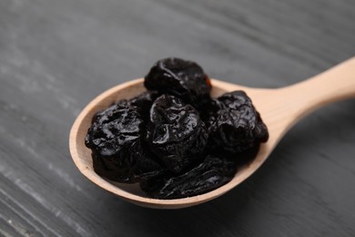 Photo of Sweet dried prunes in spoon on grey wooden table, closeup