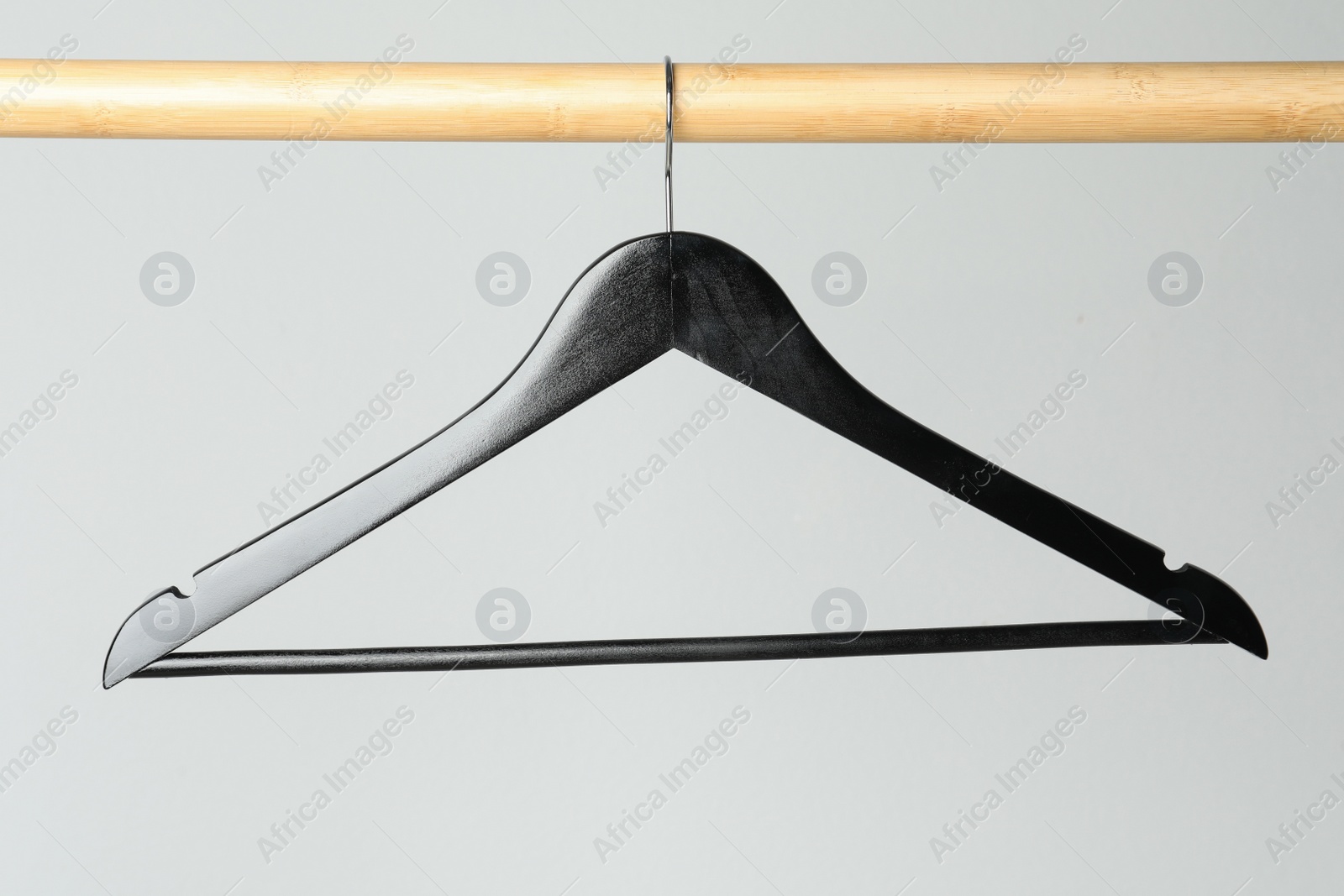 Photo of Black clothes hanger on wooden rail against light grey background