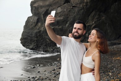 Happy young couple taking selfie on beach near sea. Space for text