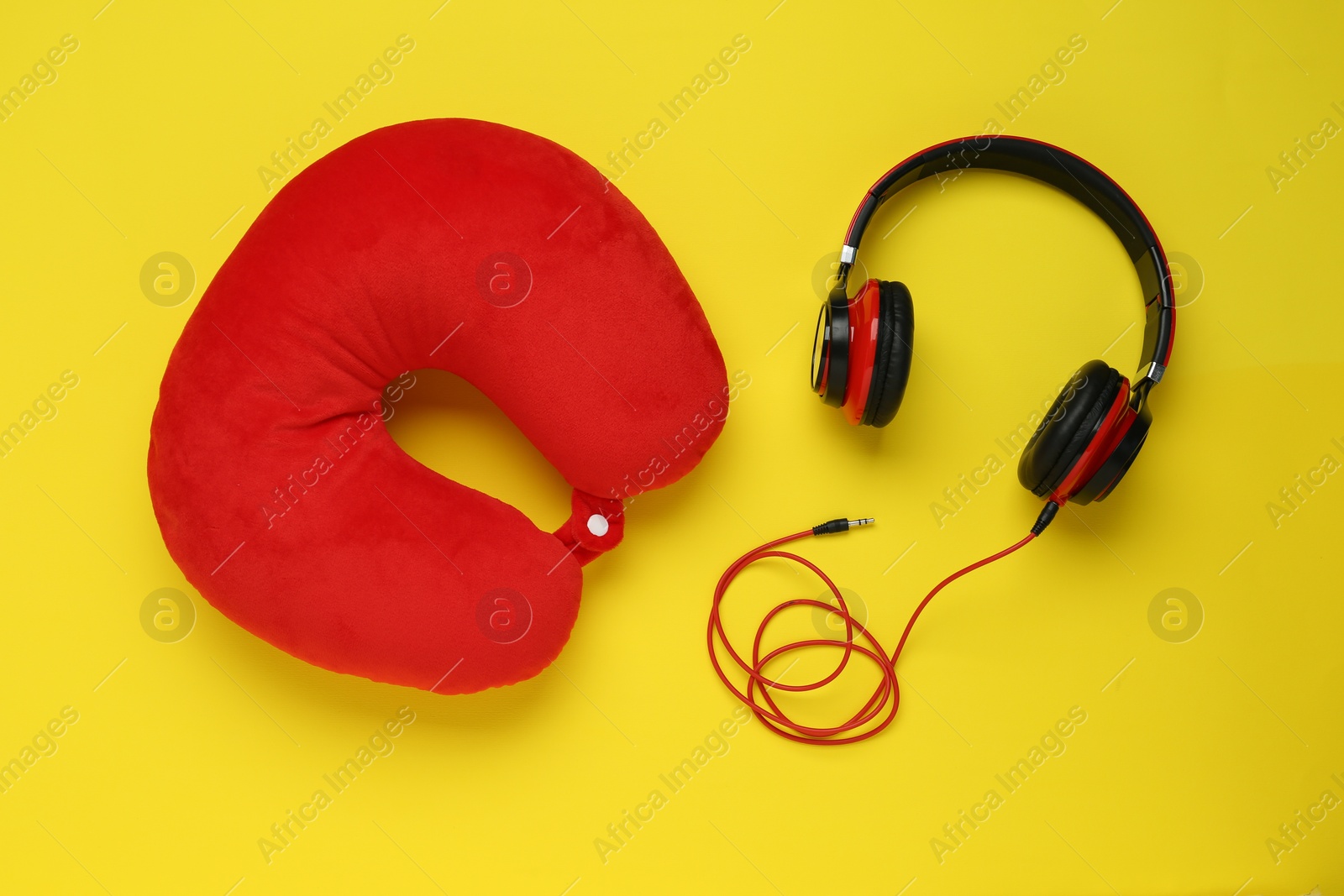 Photo of Red travel pillow and headphones on yellow background, flat lay