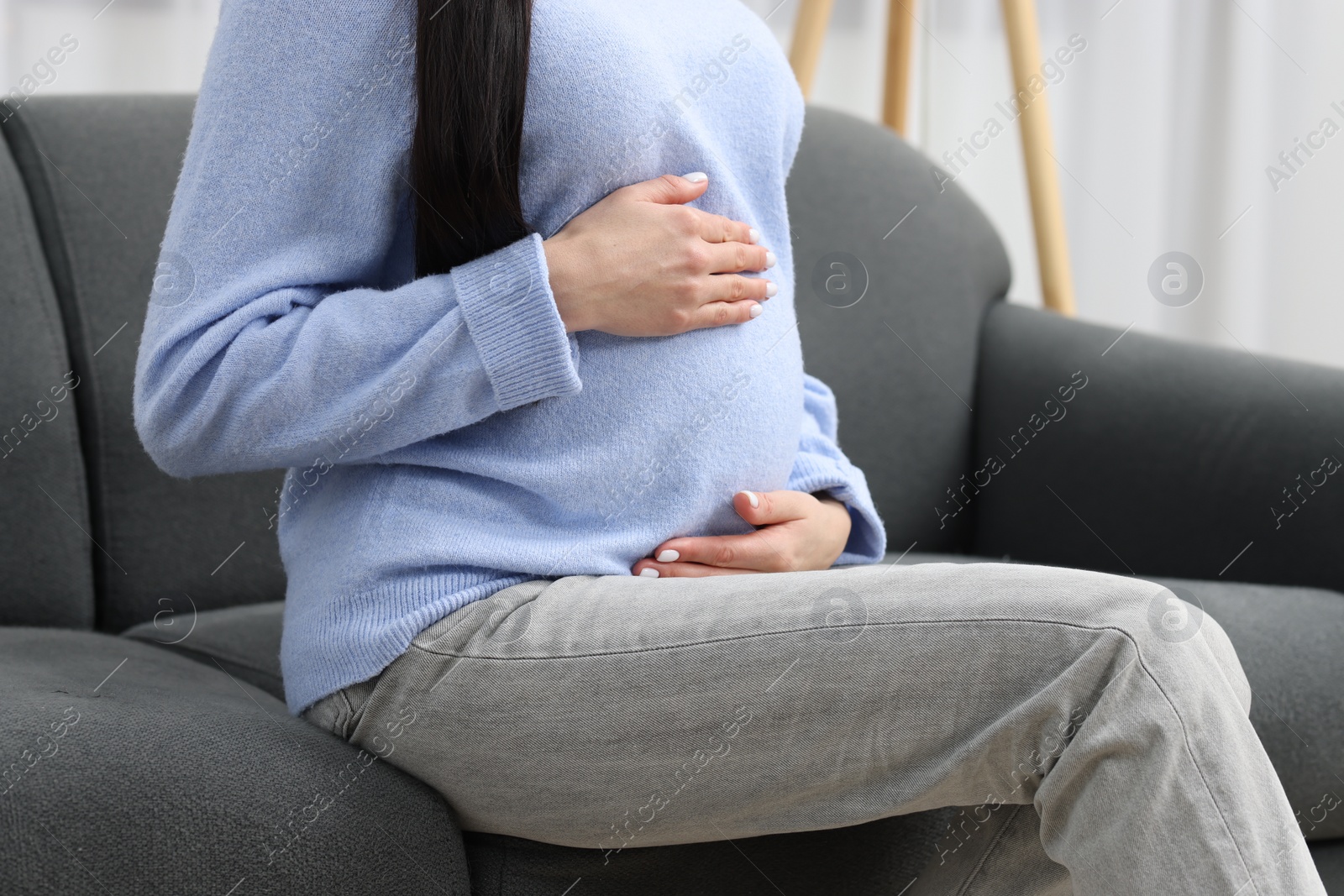 Photo of Pregnant woman touching her belly on sofa at home, closeup