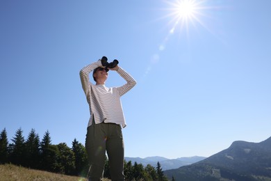 Photo of Woman looking through binoculars in mountains on sunny day, low angle view